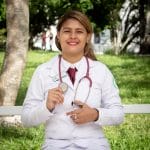 smiling woman in white long sleeve shirt with stethoscope on her neck